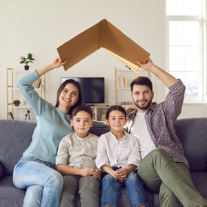 Happy family of four sitting on a couch, with parents holding a book above their heads like a roof symbolizing Estate Planning For Families With Young Children In Texas - The Law Office Of Aurelio Garza PLLC