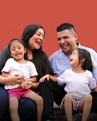 A family of four sitting together on a brick wall, enjoying a sunny day and sharing smiles and laughter.